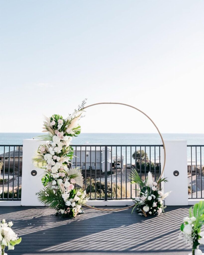 Circular gold wedding arch with white flowers overlooking the blue ocean coast