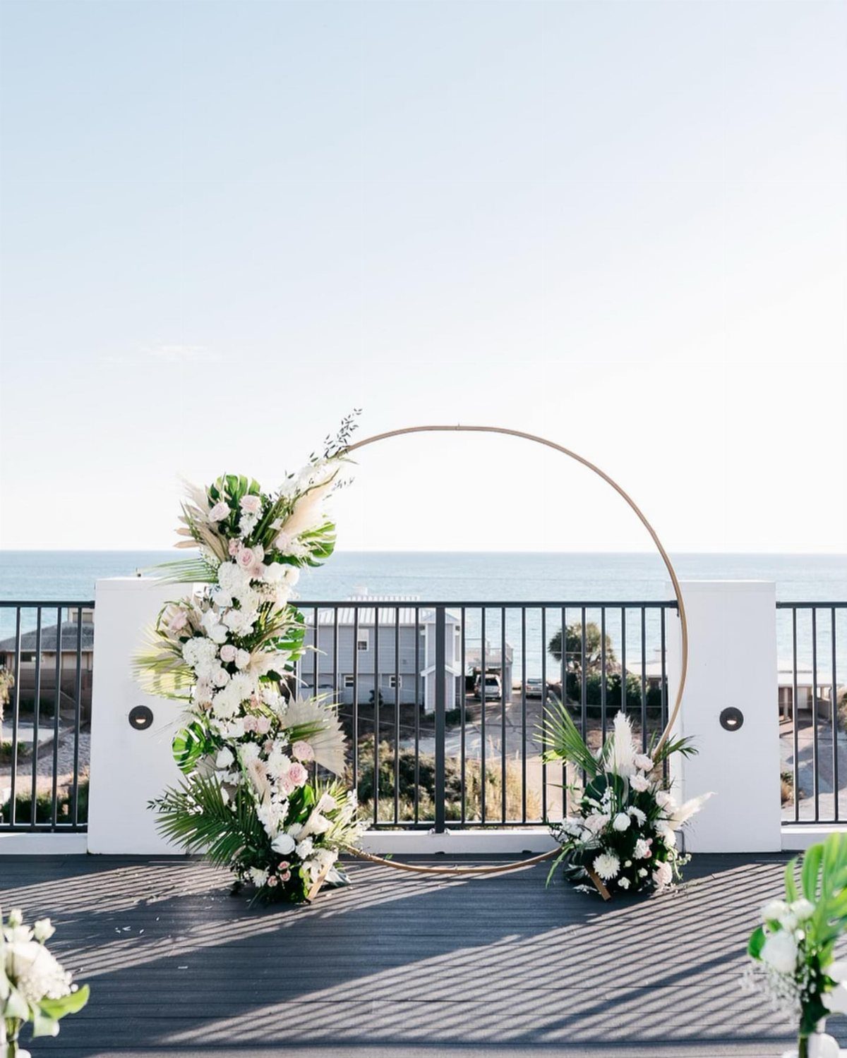 Circular gold wedding arch with white flowers overlooking the blue ocean coast