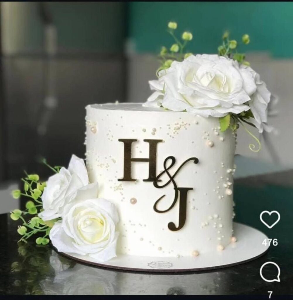White single-tier wedding cake decorated with white roses and black initials H&J.