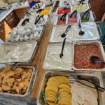 Baked potato and taco bar with foil-wrapped potatoes, chips, shells, and toppings.
