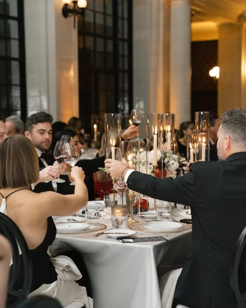 Guests in formal wear dining at a decorated table in an elegant venue.