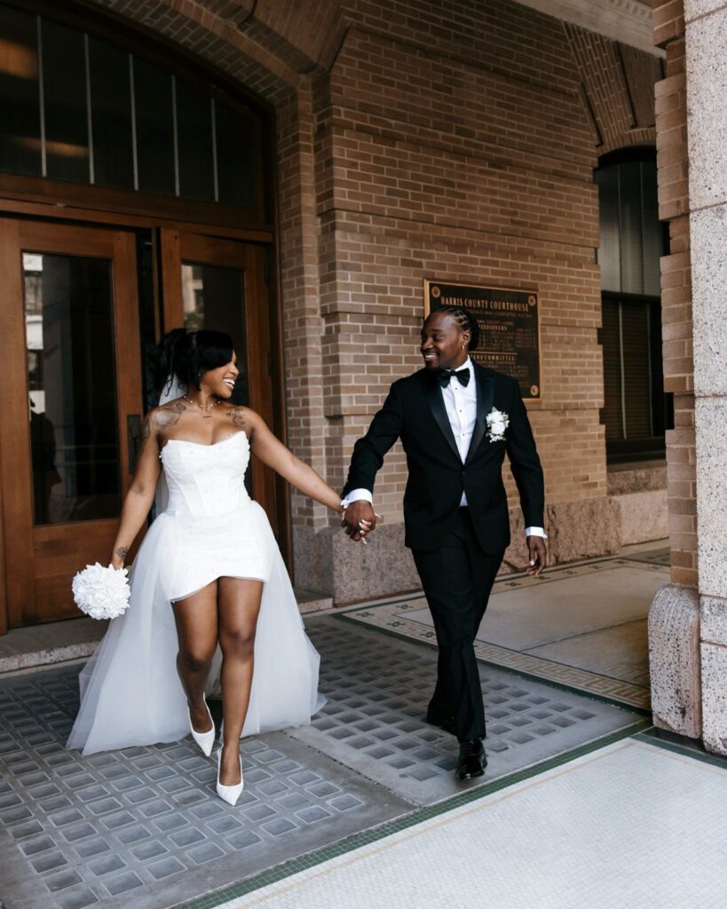Bride and groom holding hands while walking out of a brick courthouse building.