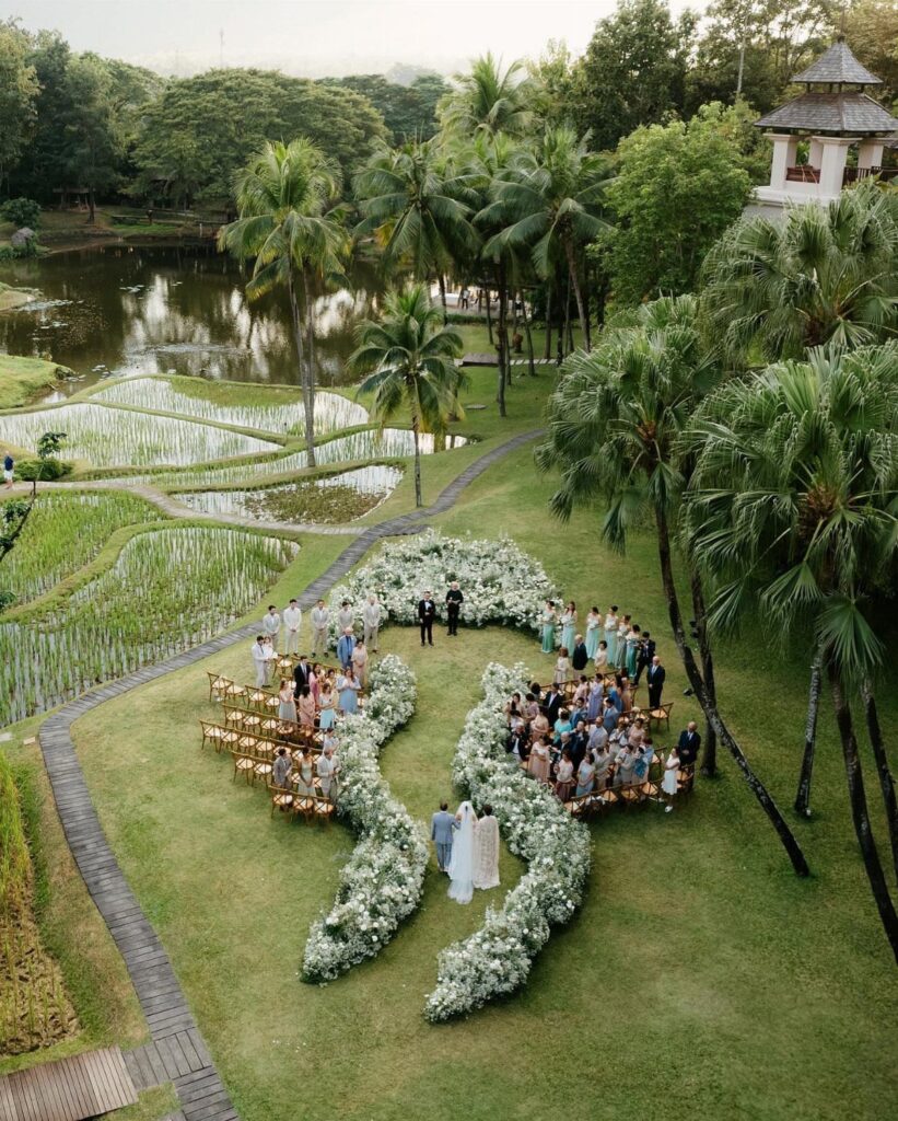 Outdoor wedding ceremony with floral arrangements set amidst tropical palm trees and rice terraces.