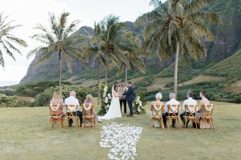 Wedding ceremony with a small guest list seated outdoors among palm trees.