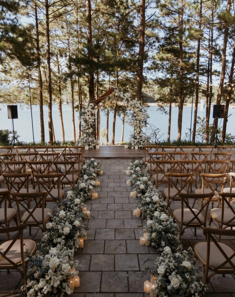 Outdoor wedding ceremony setup with floral aisle and arch overlooking a calm lake
