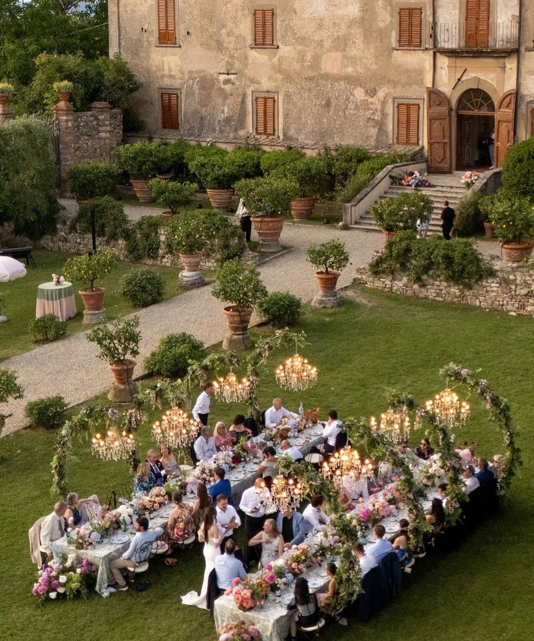 Outdoor wedding reception with a long decorated table and chandeliers in a garden