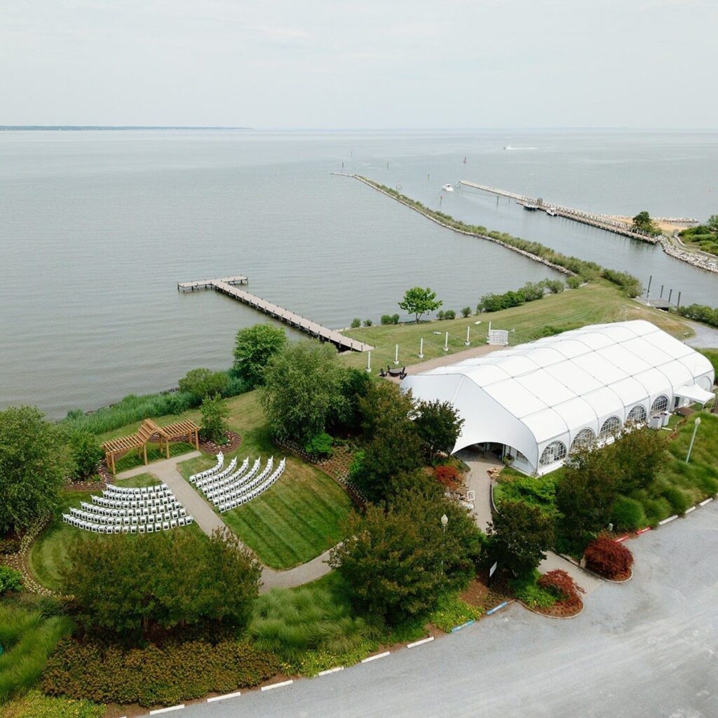 Waterfront wedding venue with a white tent and ceremony seating beside the bay.