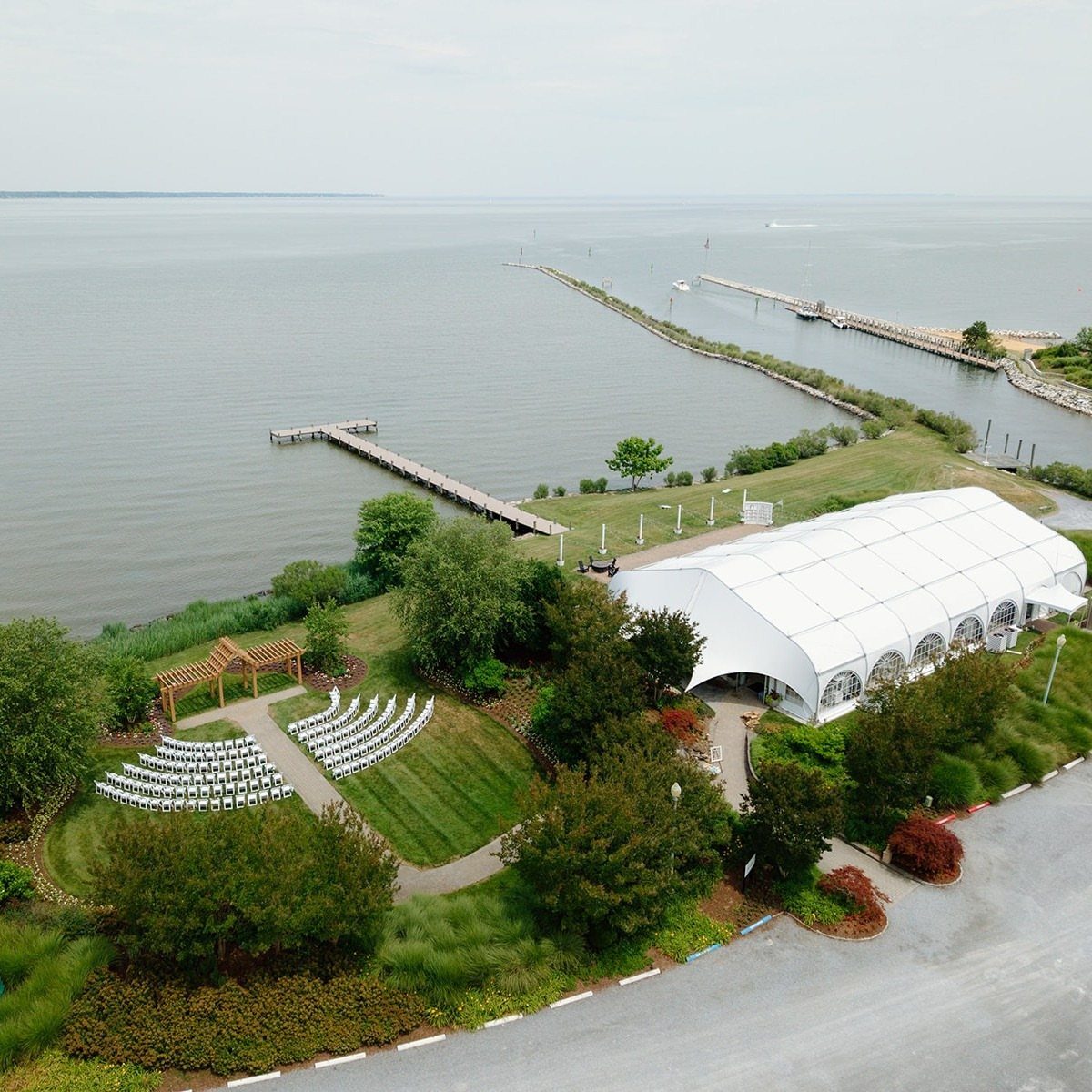 Waterfront wedding venue with a white tent and ceremony seating beside the bay.