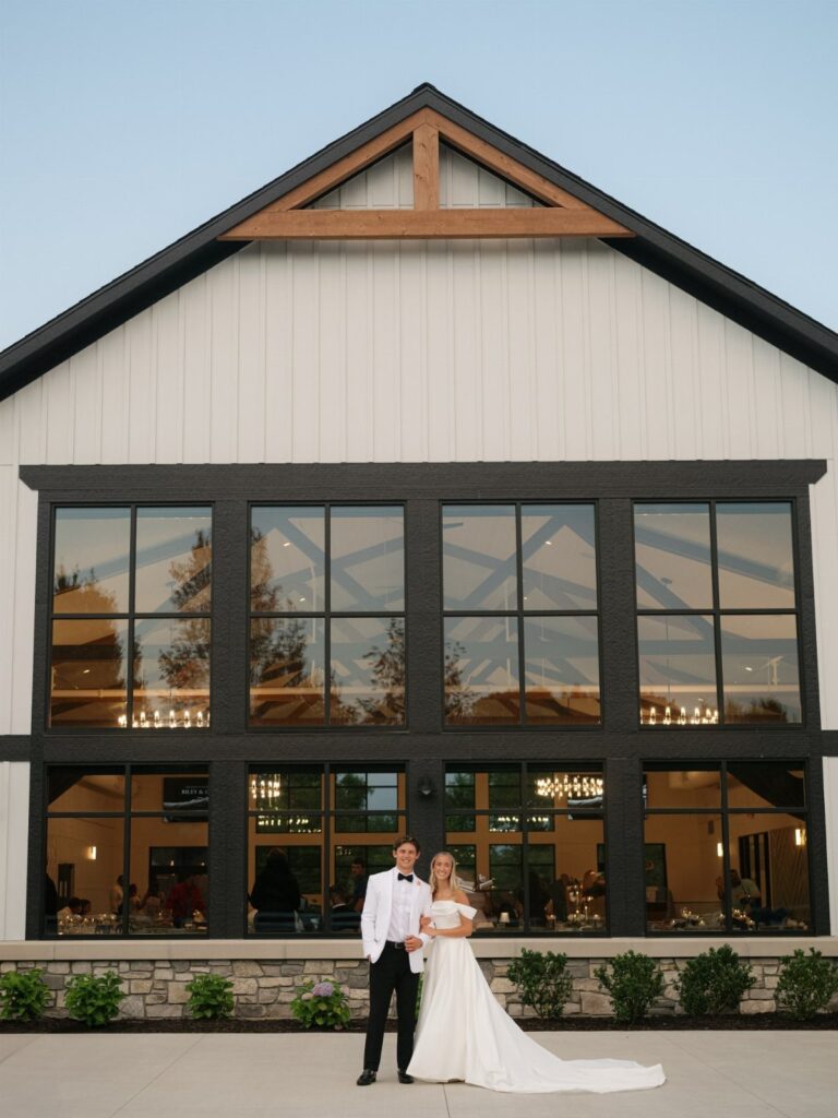 Bride and groom posing in front of a modern white wedding barn venue.