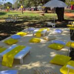 Outdoor picnic setup with yellow checkered blanket, low white tables, and yellow cushions.