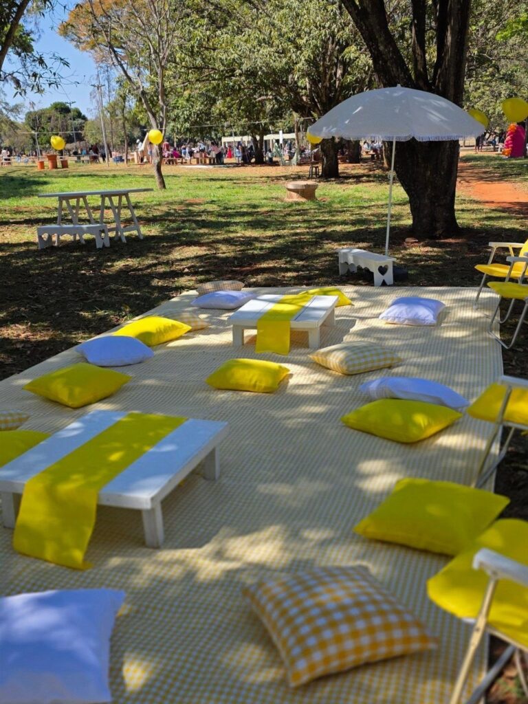 Outdoor picnic setup with yellow checkered blanket, low white tables, and yellow cushions.