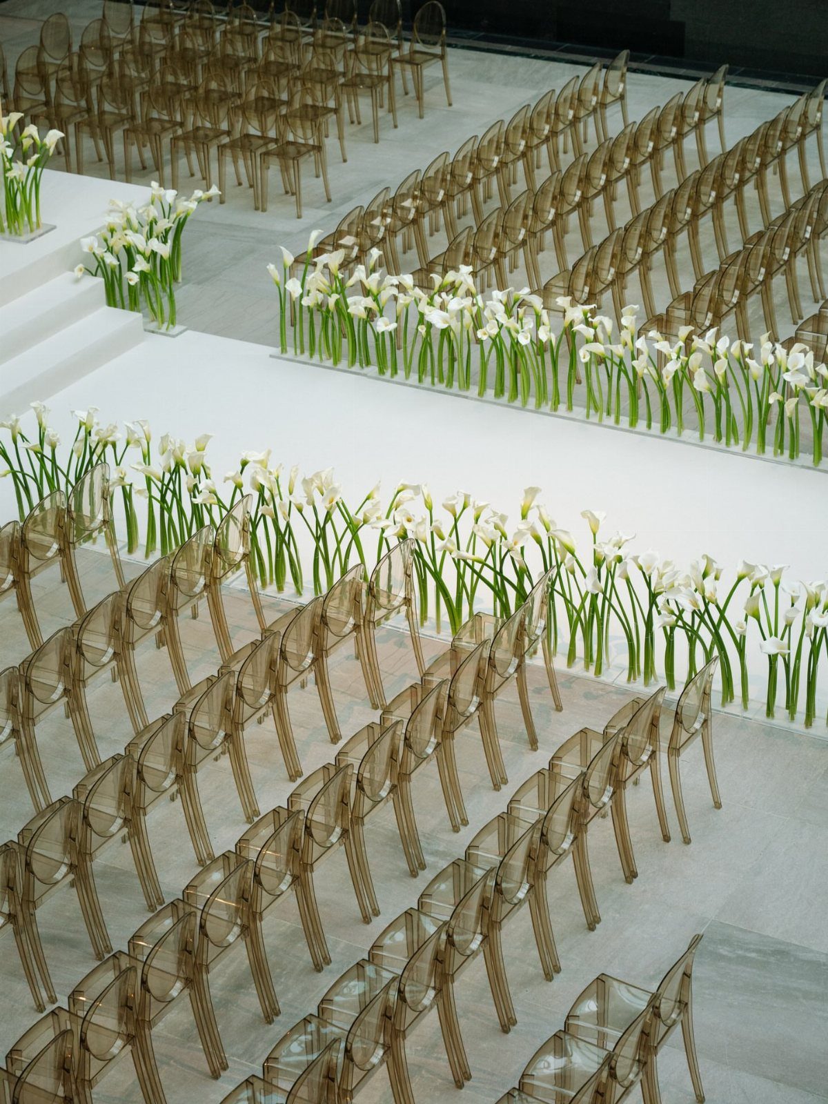 Transparent gold acrylic chairs and white calla lilies in a modern wedding setup.
