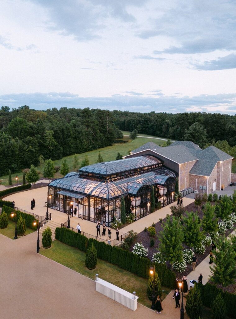 Modern wedding venue with a glass conservatory and stone building surrounded by greenery.