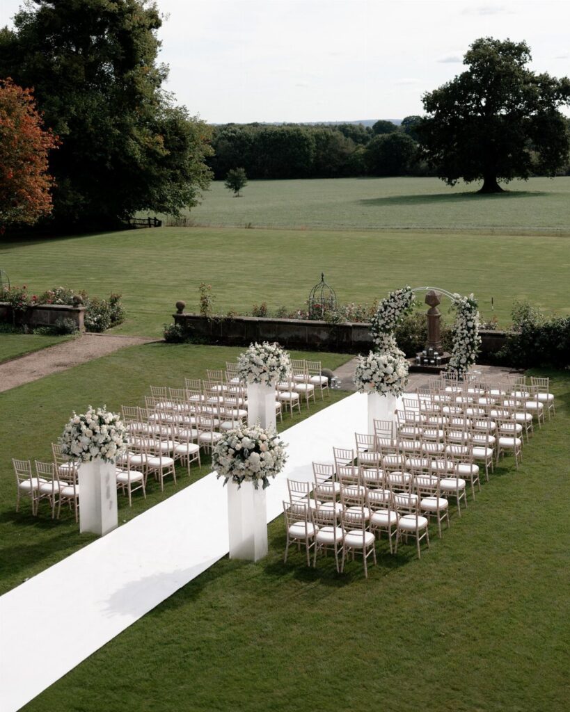 White wedding ceremony setup with aisle runner and floral arrangements on green grass