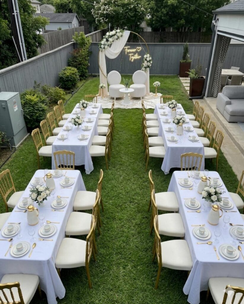 Outdoor wedding reception setup with white tables, gold chairs, and a floral arch.