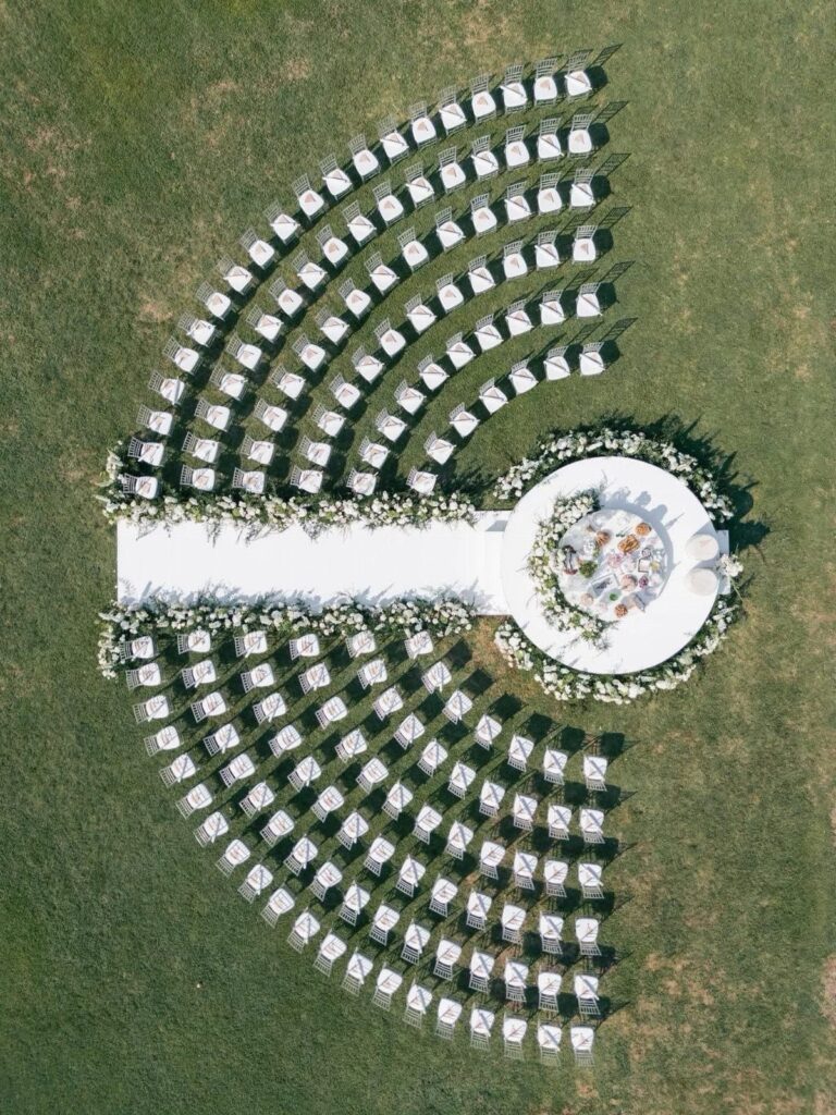 Curved rows of white chairs facing a circular floral altar on green grass.