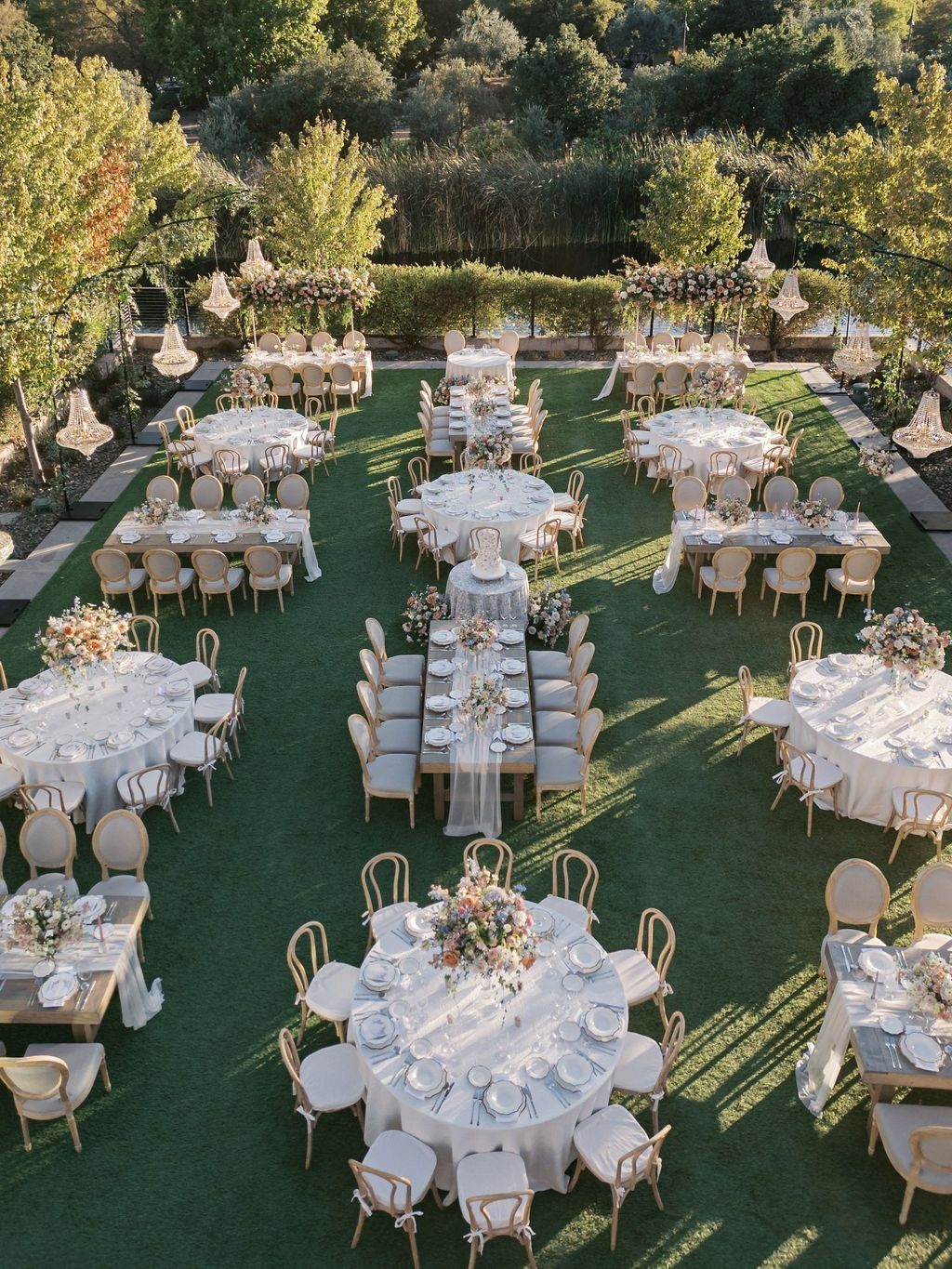 Outdoor wedding reception with white clothed tables and beige chairs on a green lawn