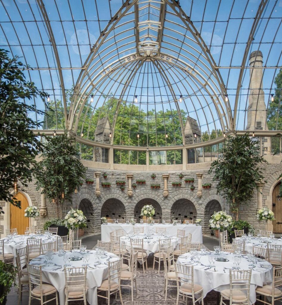 Grand glass conservatory venue set up with white tables and floral centerpieces