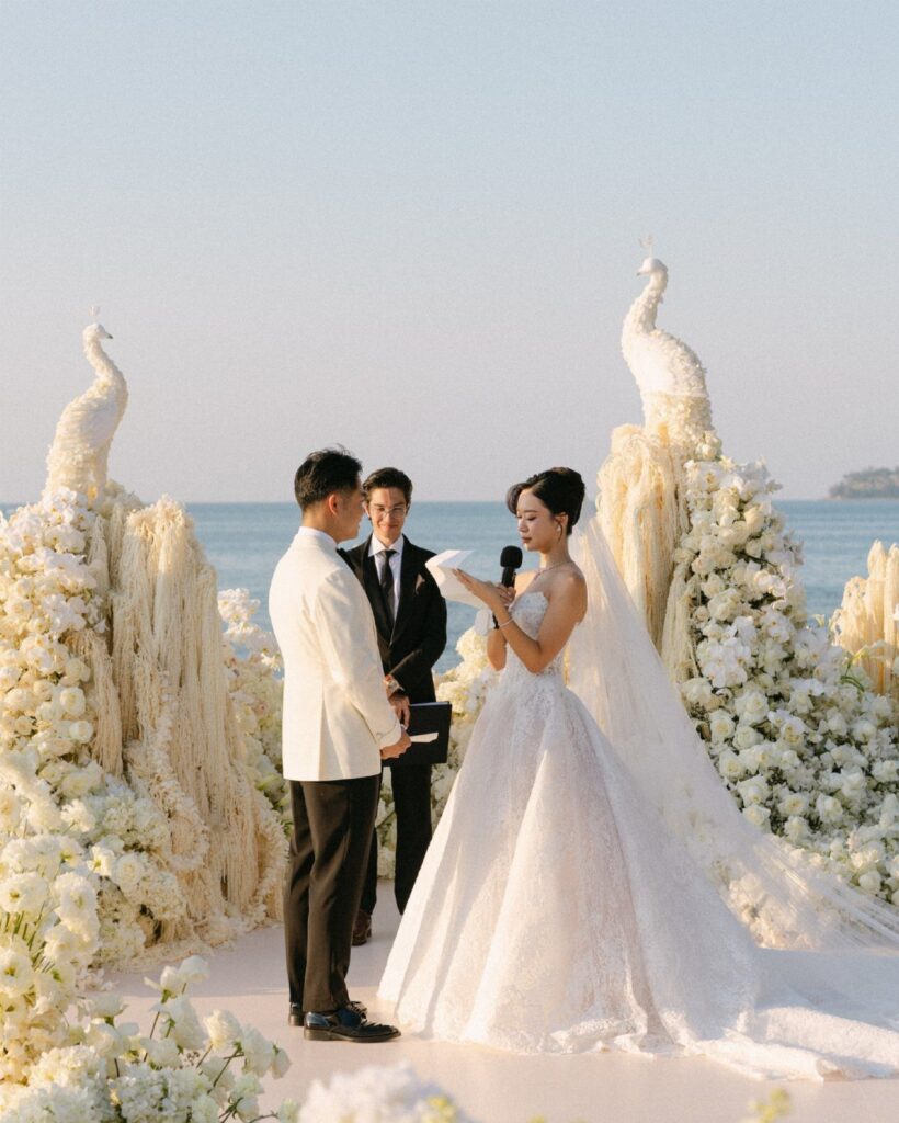 Bride and groom standing at a beach wedding ceremony with white floral decorations.