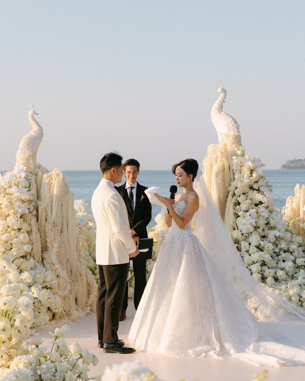 Bride and groom standing at a beach wedding ceremony with white floral decorations.