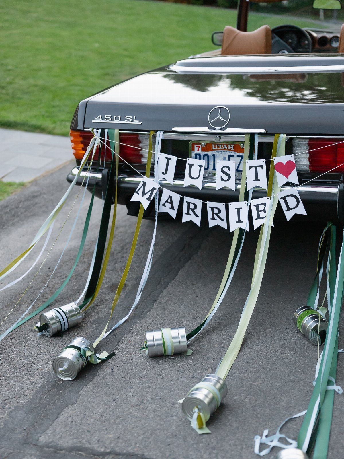 Black Mercedes convertible with Just Married banner and cans trailing behind on road