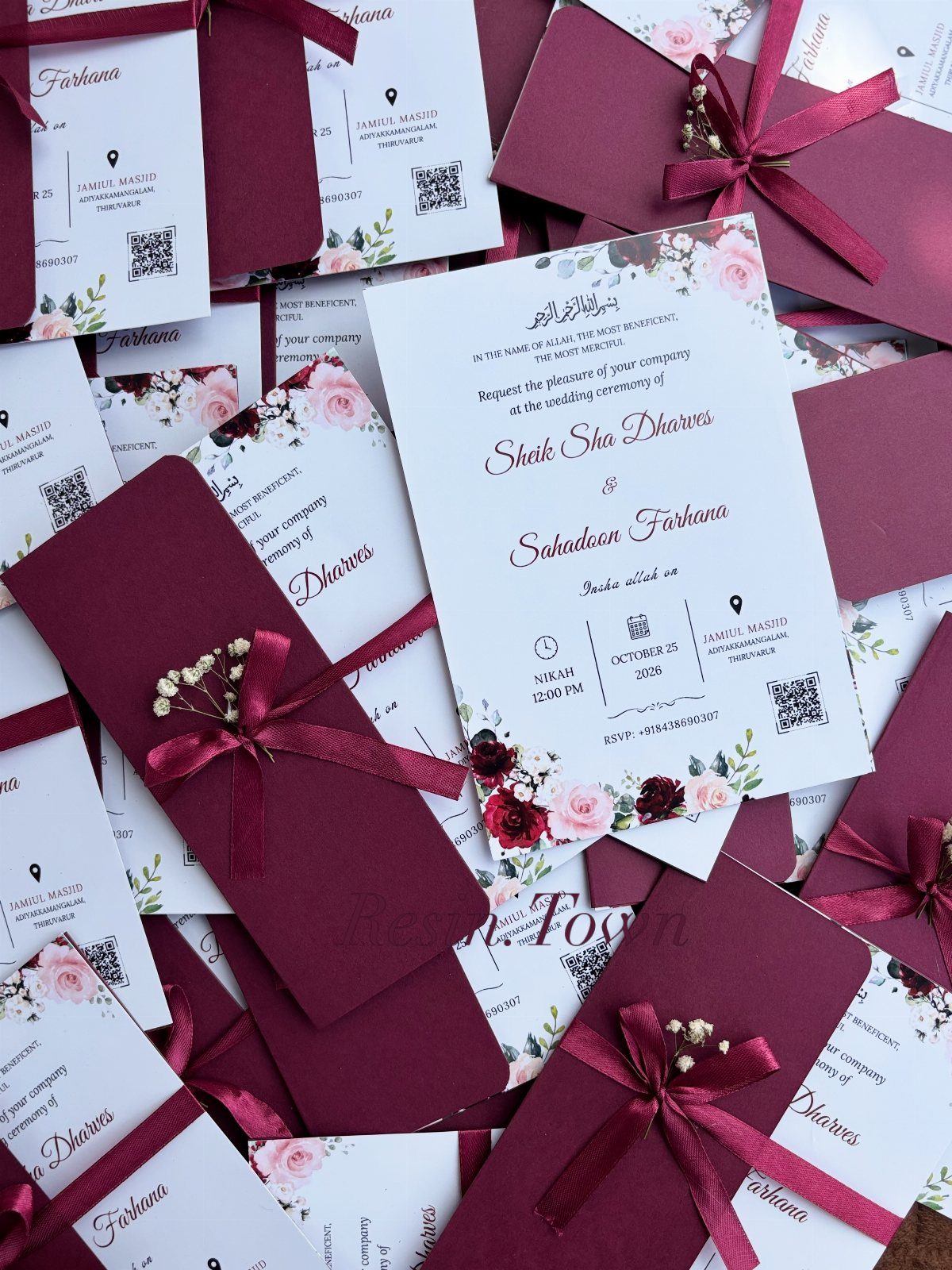 Wedding invitations with red floral designs and burgundy envelopes tied with ribbons.
