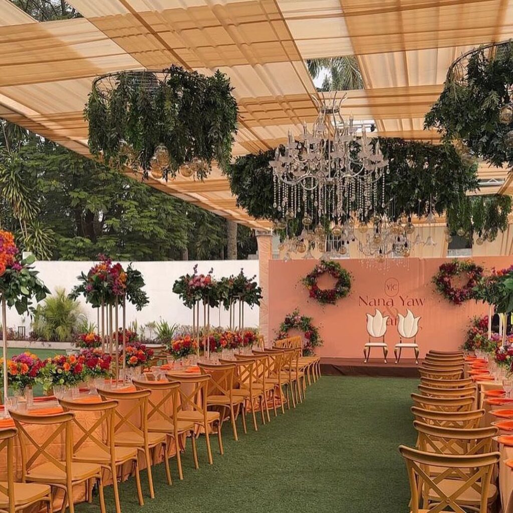 Outdoor wedding venue with a fabric canopy, crystal chandelier, and floral table settings.