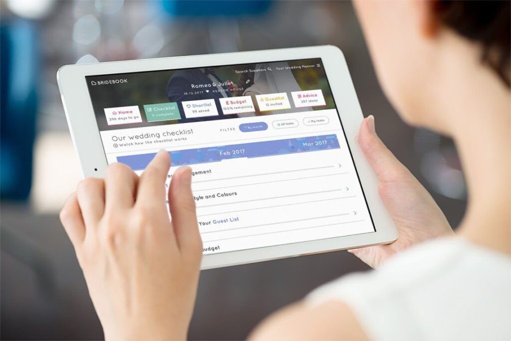Hands holding a tablet displaying the Bridebook wedding planning checklist and dashboard.