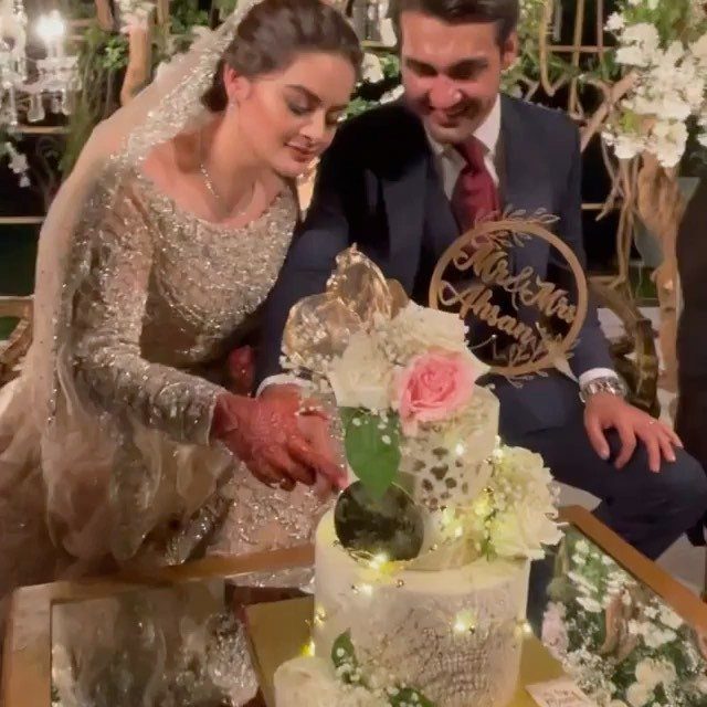 Bride and groom cutting a white tiered wedding cake decorated with fresh flowers.
