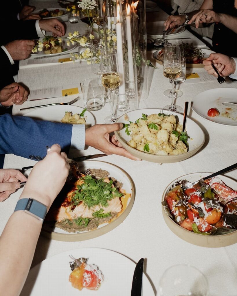 Shared bowls of roasted vegetables and cauliflower on a white wedding dinner table.