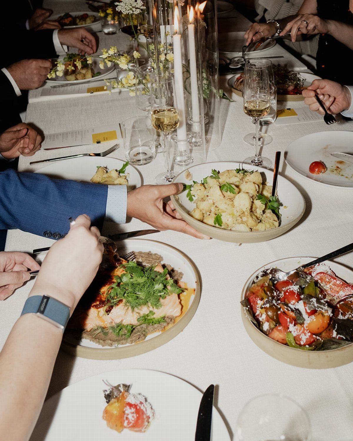 Shared bowls of roasted vegetables and cauliflower on a white wedding dinner table.