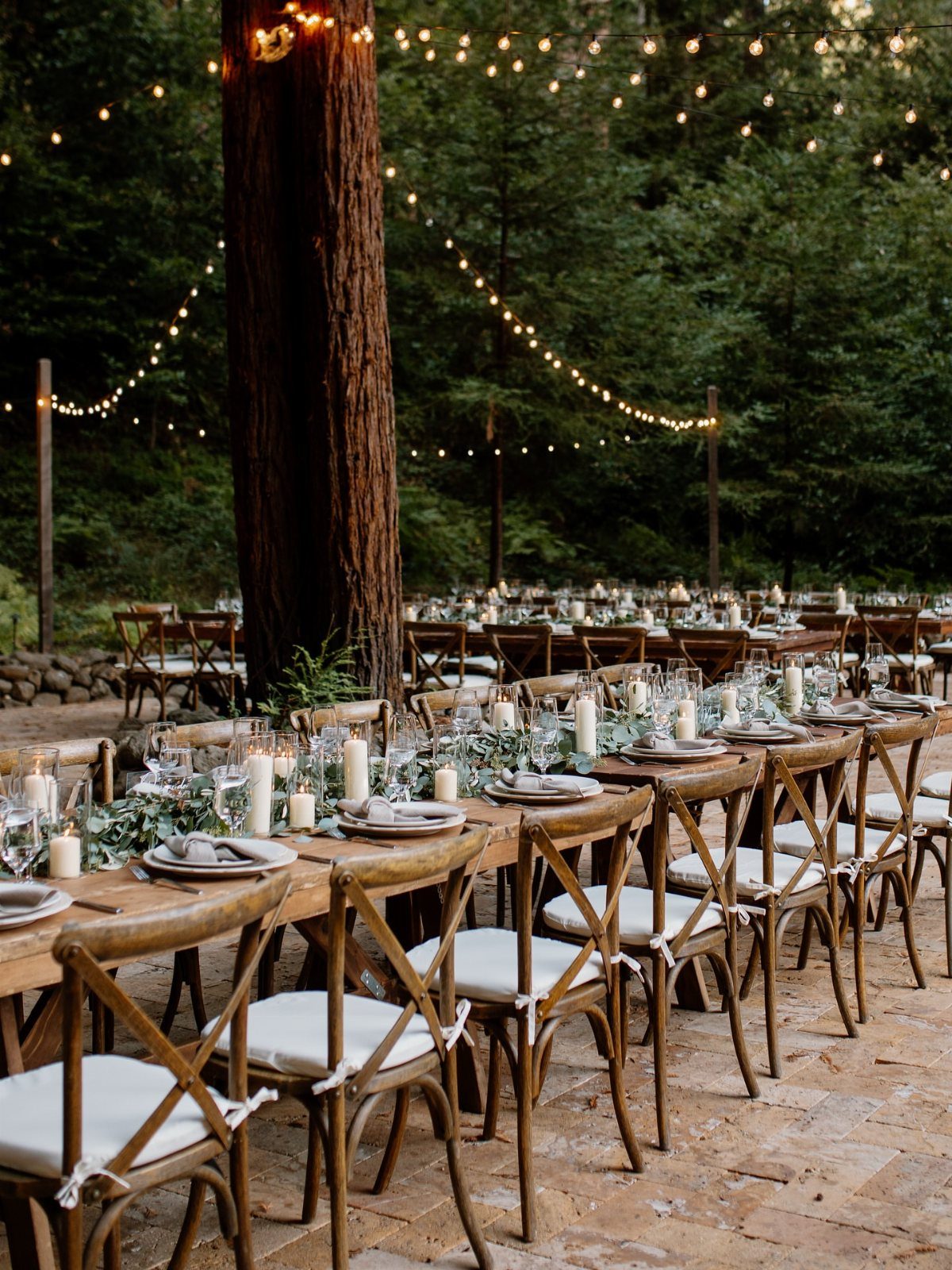 Wooden wedding tables with greenery and string lights in a lush forest setting