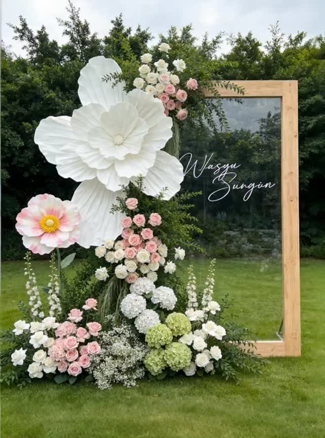 Wooden mirror frame decorated with giant white paper flowers and pastel floral arrangements.